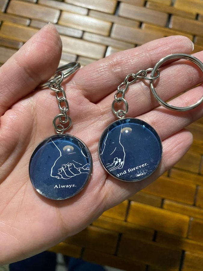 Dos llaveros azul marino con manos dibujadas, uno dice «Always» y el otro «and forever».